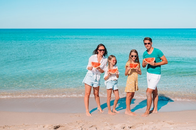 Happy family with watermelon on the beach. Parents and kids on the seashore having fun.