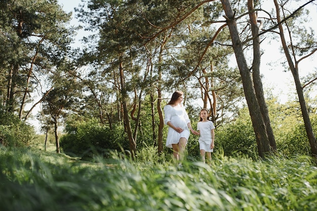 Happy family a young beautiful pregnant woman with her little cute daughter on a sunny summer day Parents and kids relationship Nature in the country