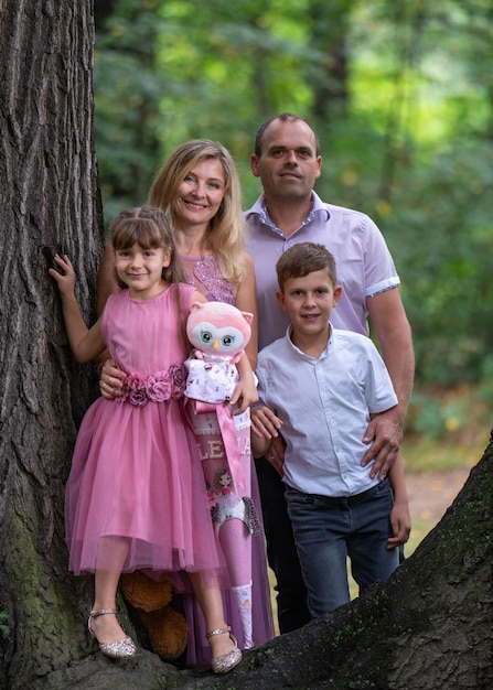 happy familyfather and motherteenage son 6 year old daughter stand near a large tree in the park