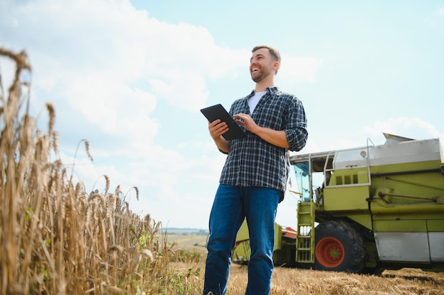 Happy farmer proudly standing in a field Combine harvester driver going to crop rich wheat harvest Agronomist wearing flannel shirt looking at camera on a farmland