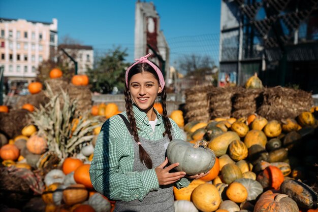 Happy farmer woman in a denim jumpsuit holds ripe pumpkin