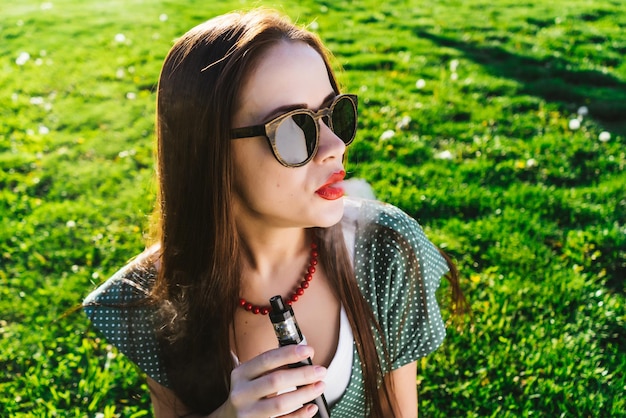 Happy fashion smiling Woman in sunglasses smoking vape on street,smoke