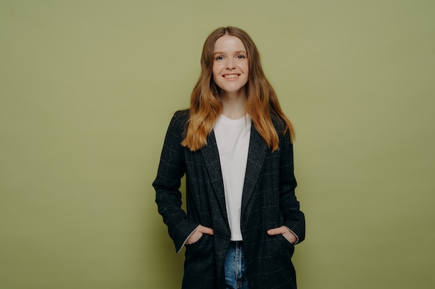 Adolescente allegro alla moda felice che indossa blazer e jeans con le mani in tasca e sorride alla macchina fotografica, giovane donna che guarda la macchina fotografica con espressione felice, foto in studio