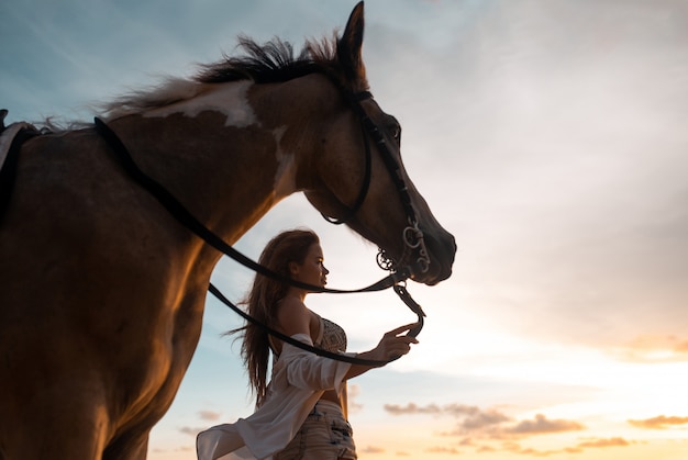 Счастливая модная молодая женщина позирует с лошадью на пляже