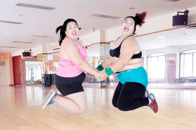 Happy fat women jumping together in fitness center