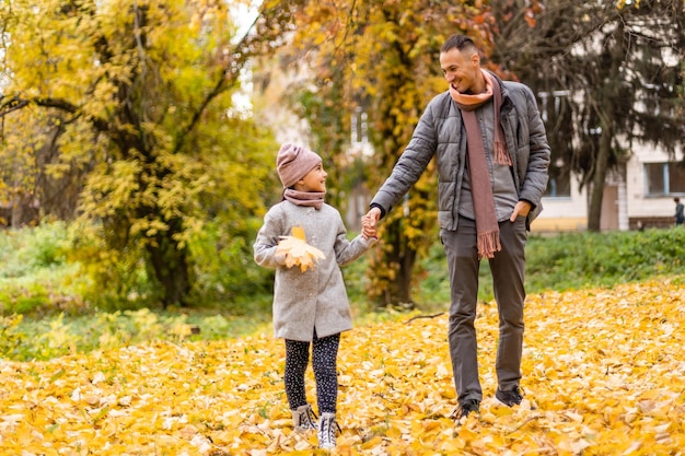 Felice padre e figlia nel parco autunnale su foglie gialle