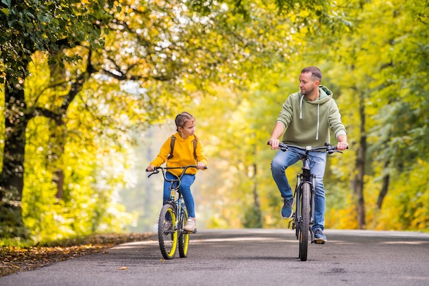 Felice padre e figlia vanno in bicicletta nel parco autunnale in una giornata di sole
