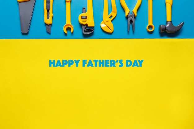 Happy Father Day-tag met speelgoedgereedschap op blauwe gele achtergrond bovenaanzicht met kopie ruimte voor tekst.