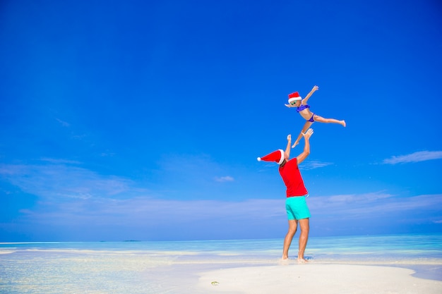 Happy father and his adorable little daughter in Santa Hat at tropical beach 