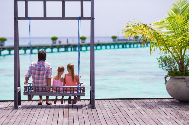 Happy father and his adorable little daughters at tropical beach having fun