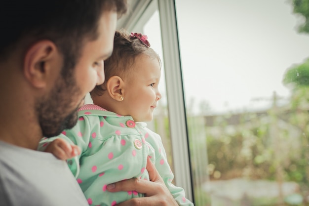 Photo happy father holding his charming baby daughter in front of a window