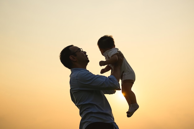 Happy father holding newborn baby playing together with sunset view