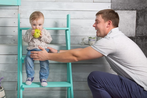 幸せな父は息子と一緒に大きな青リンゴを食べる男の子を抱きます屋内の階段に座っています