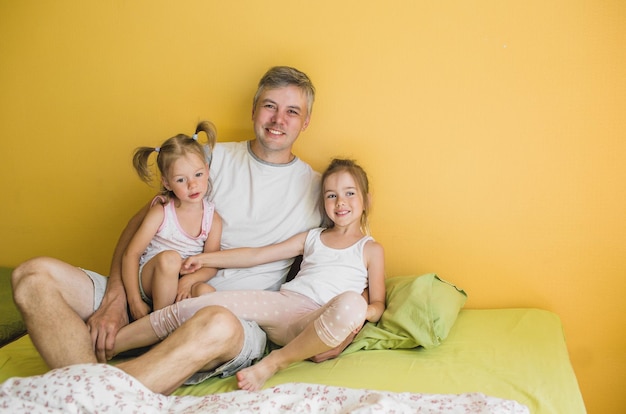 A happy father is playing in bed with two young daughters. joy care family vacation