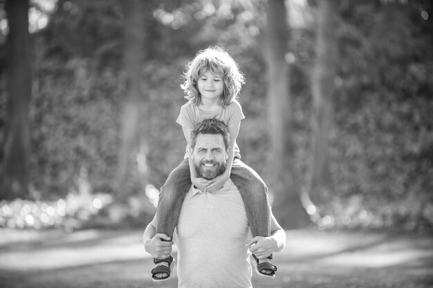 Happy father man carry boy child sitting on fathers shoulders summer outdoors piggyback