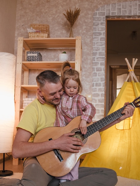 행복한 아버지는 어린 딸을 위해 기타를 연주합니다. 아이들의 보살핌과 교육