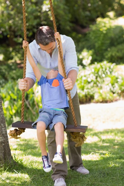 Счастливый отец толкает мальчика на качели
