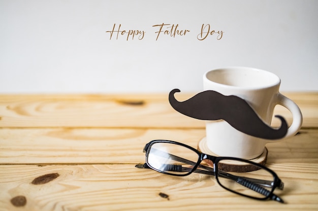 Foto concetto di festa del papà felice. una carta per baffi neri, una tazza di caffè e bicchieri su un tavolo di legno.