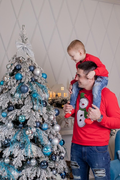 Happy Father and son enjoying decorating Christmas tree with Christmas balls and light garland preparing for celebrating winter holidays Merry Christmas Eve and Happy New Year 2021 Family concept