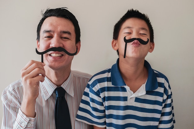 Happy father and son having fun with fake mustache