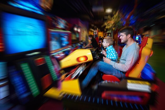 Happy father and son playing driving wheel video game in playground theme park