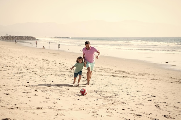 Happy father and son playing football having fun on summer sandy beach family vacation parenthood