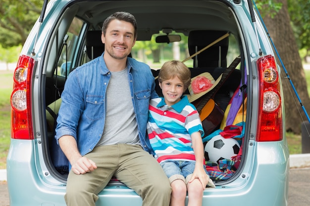 Happy father and son sitting in car trunk