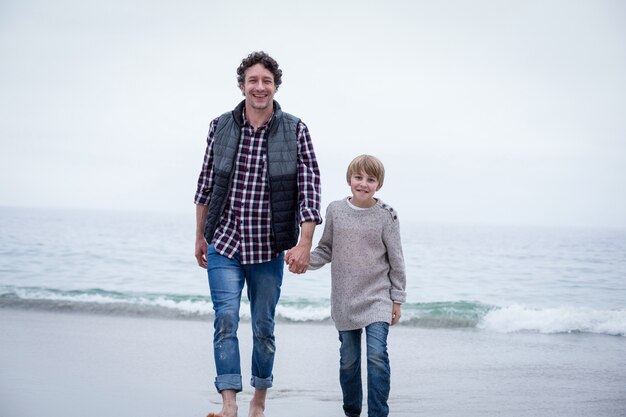 Happy father and son walking at sea shore against sky