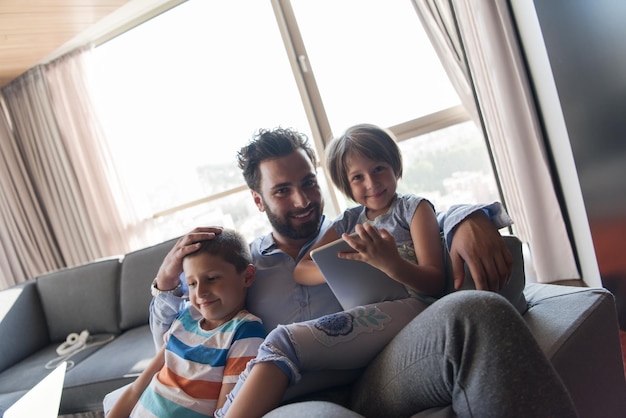 happy father spending time with kids using tablet computer on an armchair at home