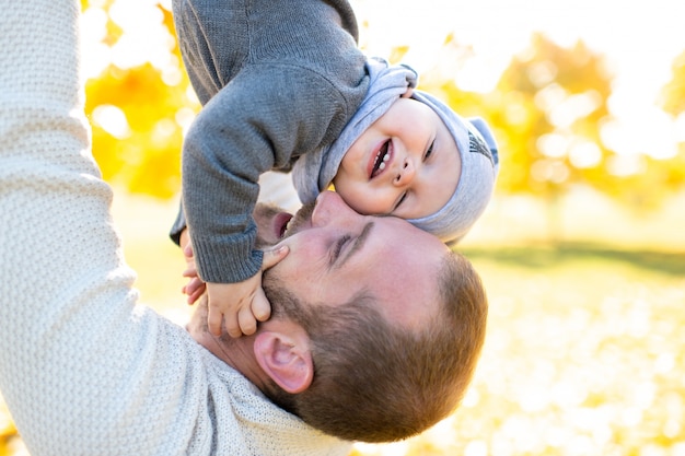 Happy father throws his adorable baby up in autumn park.