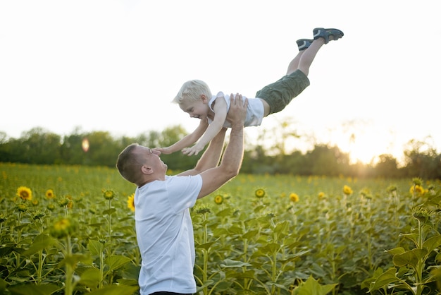 Il padre felice alza il suo piccolo figlio sul giacimento dei girasoli