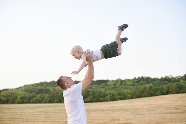 Счастливый отец подбрасывает маленького белокурого мальчика на скошенном пшеничном поле. Время заката