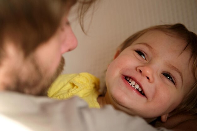 娘と幸せな父 小さな女の子 1 歳の赤ちゃん 笑顔 笑うパパを見上げる 男 子供に愛情を示す 率直な本当の感情 あごひげ お父さんと小さな子供 本物の家族のライフ スタイル