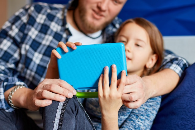 집에서 소파에 거실에서 태블릿 컴퓨터를 사용하는 딸과 함께 행복한 아버지