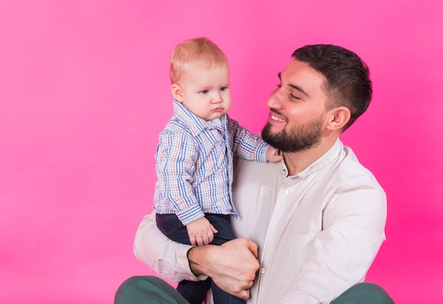 Happy father with his baby son on pink wall