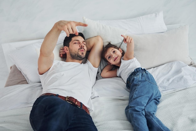 Happy father with his daughter spending free time at home together Lying down on bed