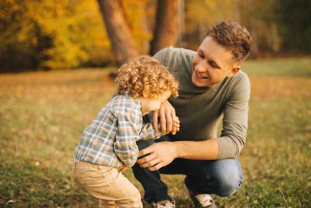 Padre felice con suo figlio piccolo sorridente all'aperto nel parco al tramonto, divertirsi insieme