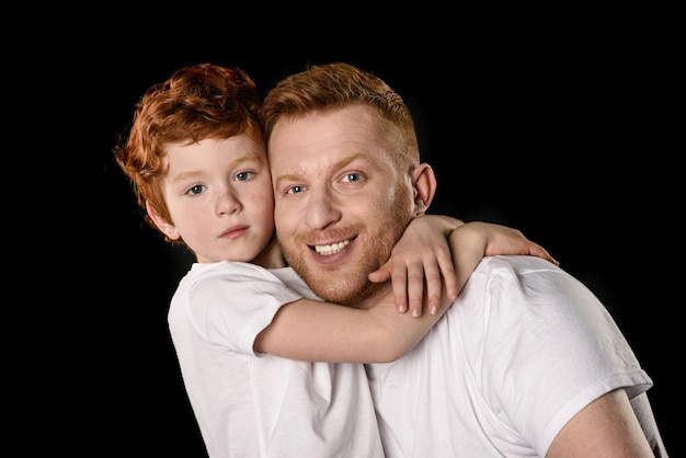 Happy father with son hugging and smiling at camera isolated on black