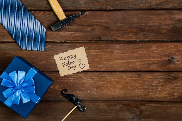 Foto happy fathers day geschenkdoos met stropdas, hamer, blauwe doos en snor op een rustieke houten achtergrond.