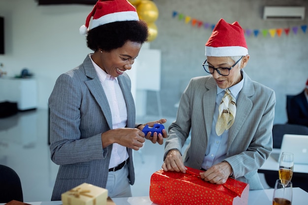 Счастливые коллеги-женщины упаковывают подарочную коробку на рождественскую вечеринку в офисе
