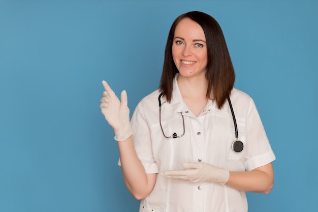 Happy female doctor in medical gloves with a stethoscope pointing to copy space