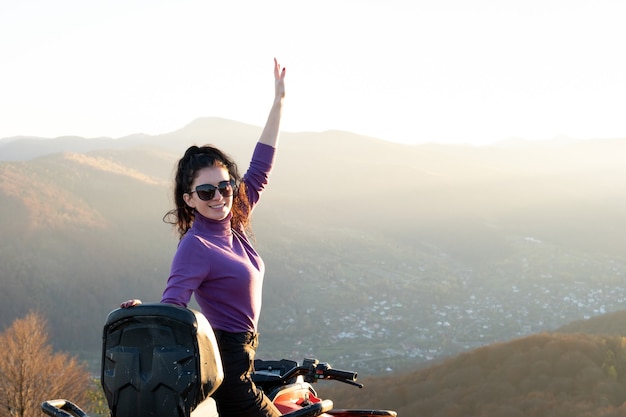 Autista femminile felice che si gode la guida fuoristrada su una moto quad atv in montagne autunnali al tramonto.