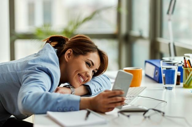 Happy female entrepreneur using smart phone and text messaging while relaxing in the office