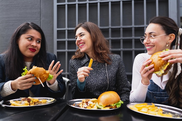 패스트 푸드에서 햄버거를 먹으면서 수다를 떠는 행복한 여자 친구들.