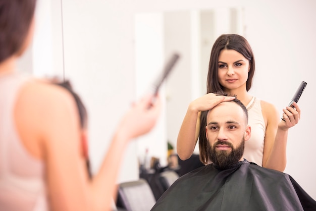 Happy female hairdresser is cutting clients hair at salon.