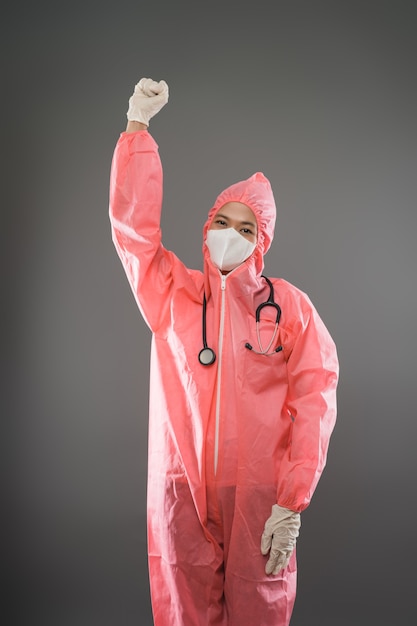 Foto felice lavoratrice medica in piedi che indossa dpi e maschera con una mano alzata