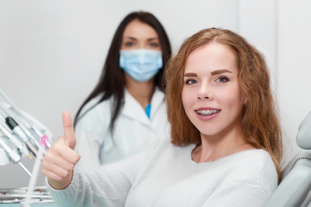 Felice paziente femminile sorridente che mostra i pollici in su seduto in poltrona odontoiatrica