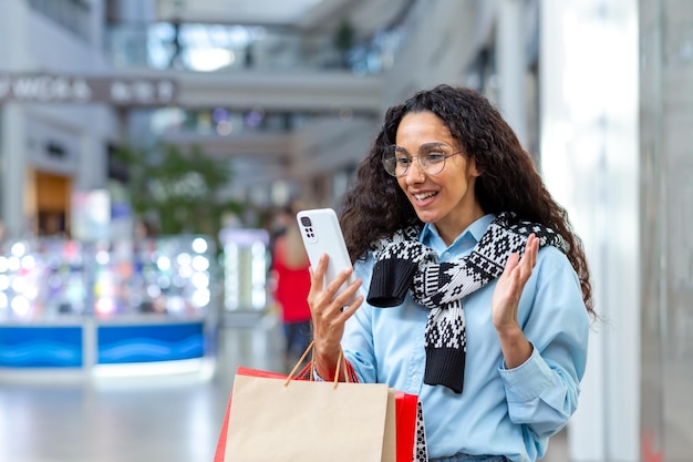 Happy female shopper inside store talking on video call with friends hispanic woman using smartphone