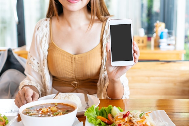 Photo happy female sitting in the restaurant and showing empty copy space smartphone