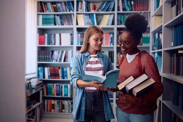 Happy female students cooperating while learning from a book in library